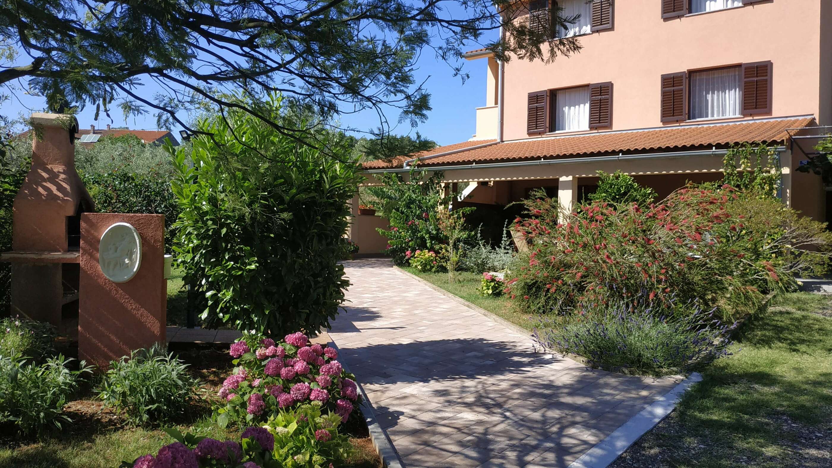 Big colorful garden with lots of flowers and plants. Large barbecue and  big sink. Access path to the apartment.