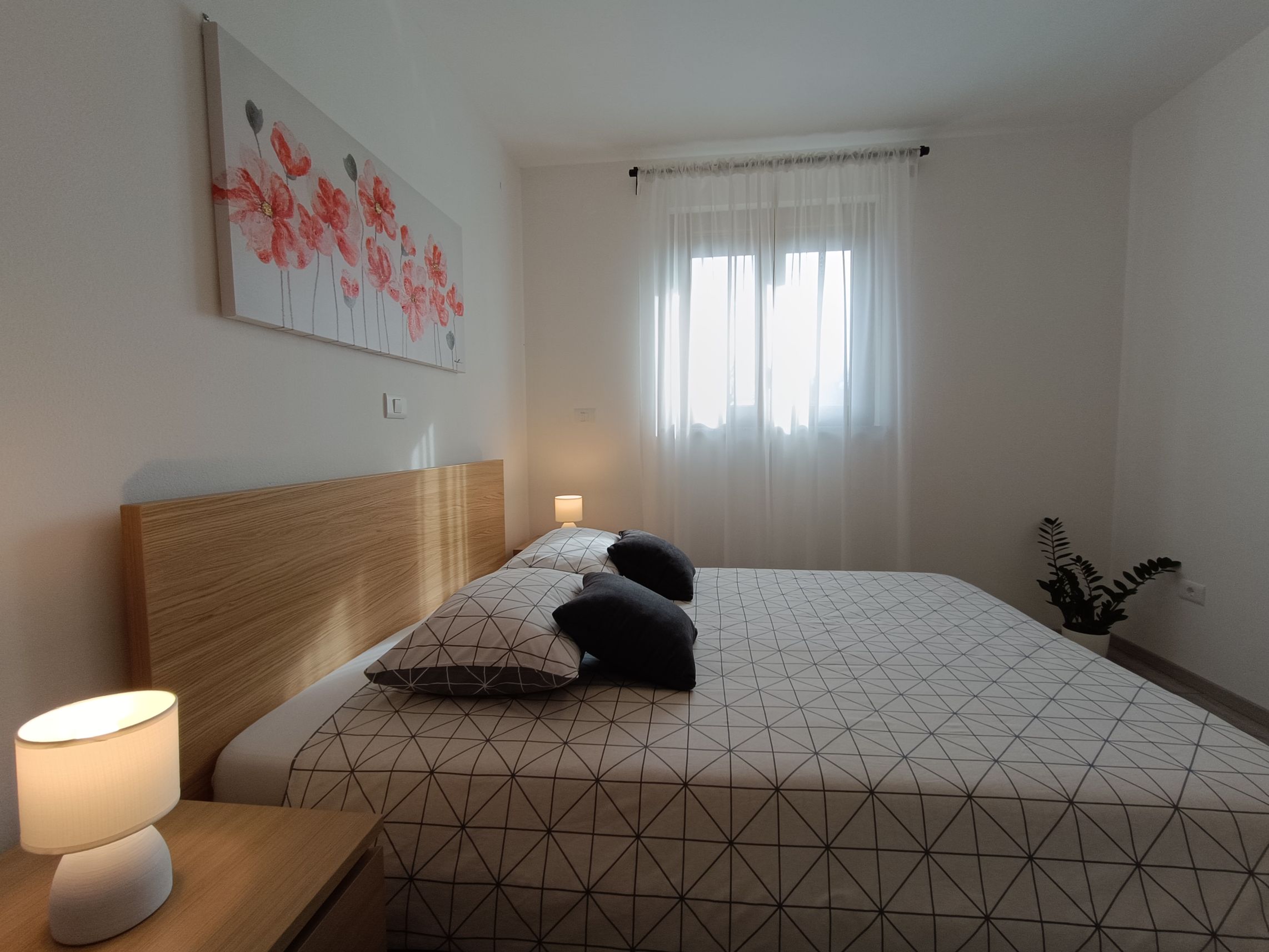 Two single beds with dimensions 90x200 in the center of a bright spacious bedroom. Colorful bedsheets and pillow linens. Lamps on night stands. Cabinet with multiple drawers and hangers alongside a luggage table. Beautiful painting on the wall.