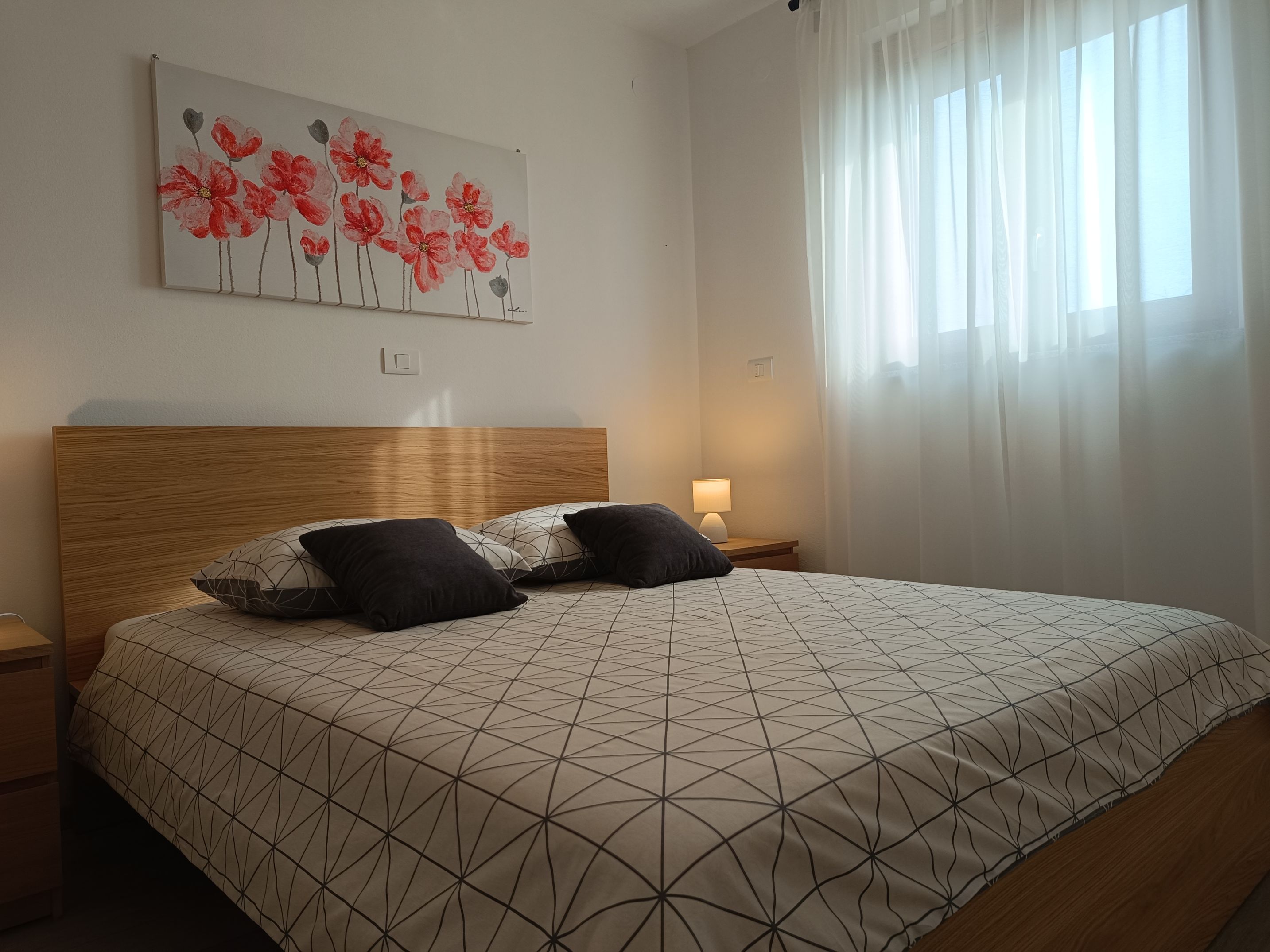Two single beds with dimensions 90x200 in the center of a bright spacious bedroom. Colorful bedsheets and pillow linens. Lamps on night stands. Cabinet with multiple drawers and hangers alongside a luggage table. Beautiful painting on a wall.