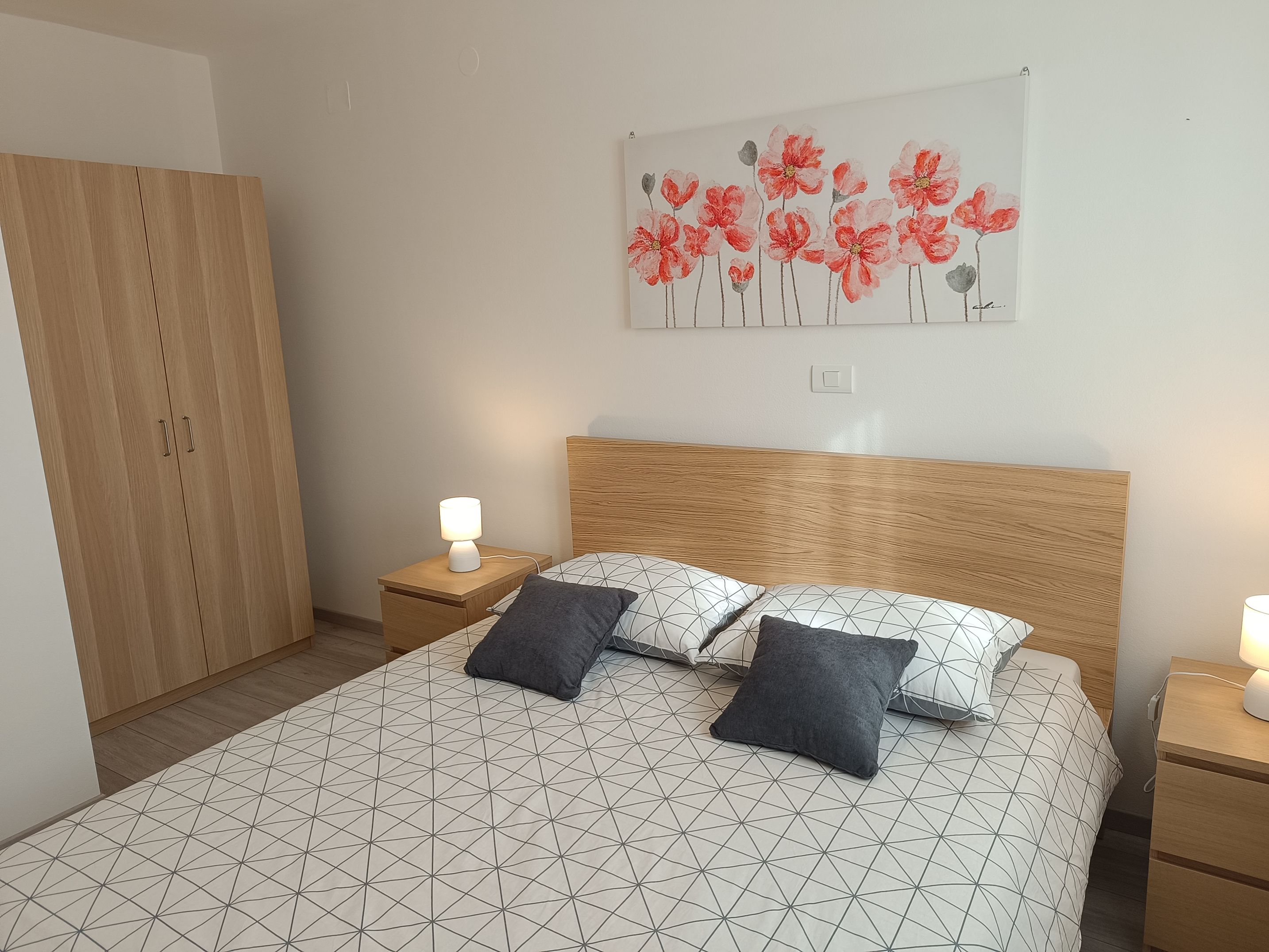 Big tiled spacious bathroom with a sink, towels, toilet, shower and radiator. Colorful towels on the hangers, radiator and towel shelf with hair dryer. Additional hangers on the wall. Toilet paper near the toilet. Shampoo in a glass shower cabin.