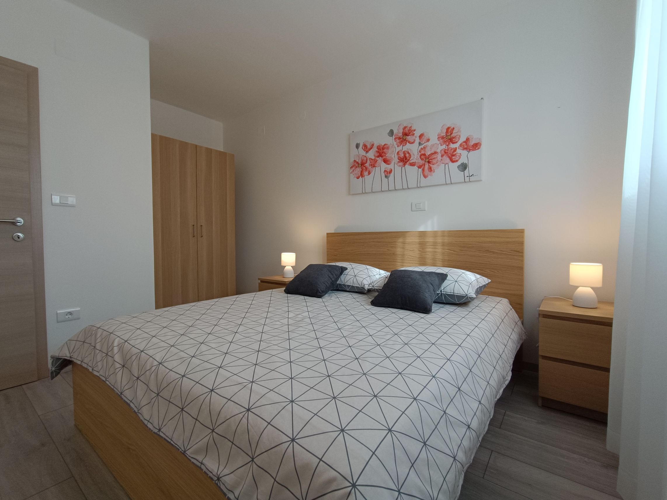 Large bright bedroom with two single beds 90x200. Two night stands near each bed and lamps on them. Beautiful colorful bedsheets and pillows. Painting on the wall. Big window which brings lots of light and chair with mirror next to it.