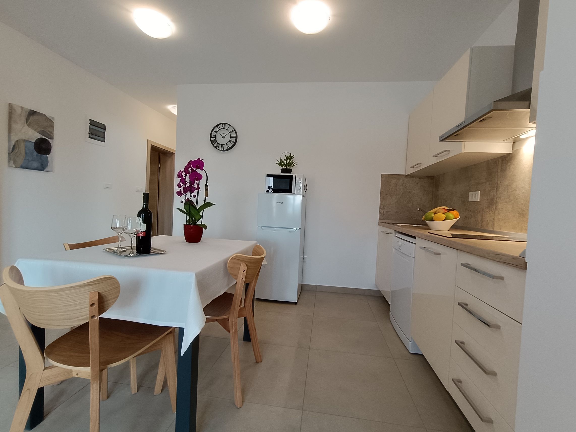 Red kitchen and bright dining room with big window. Lined dining table with tablecloth and four chairs. Big red kitchen with a big refrigerator and every possible appliance including stove, sink, and cupboards.